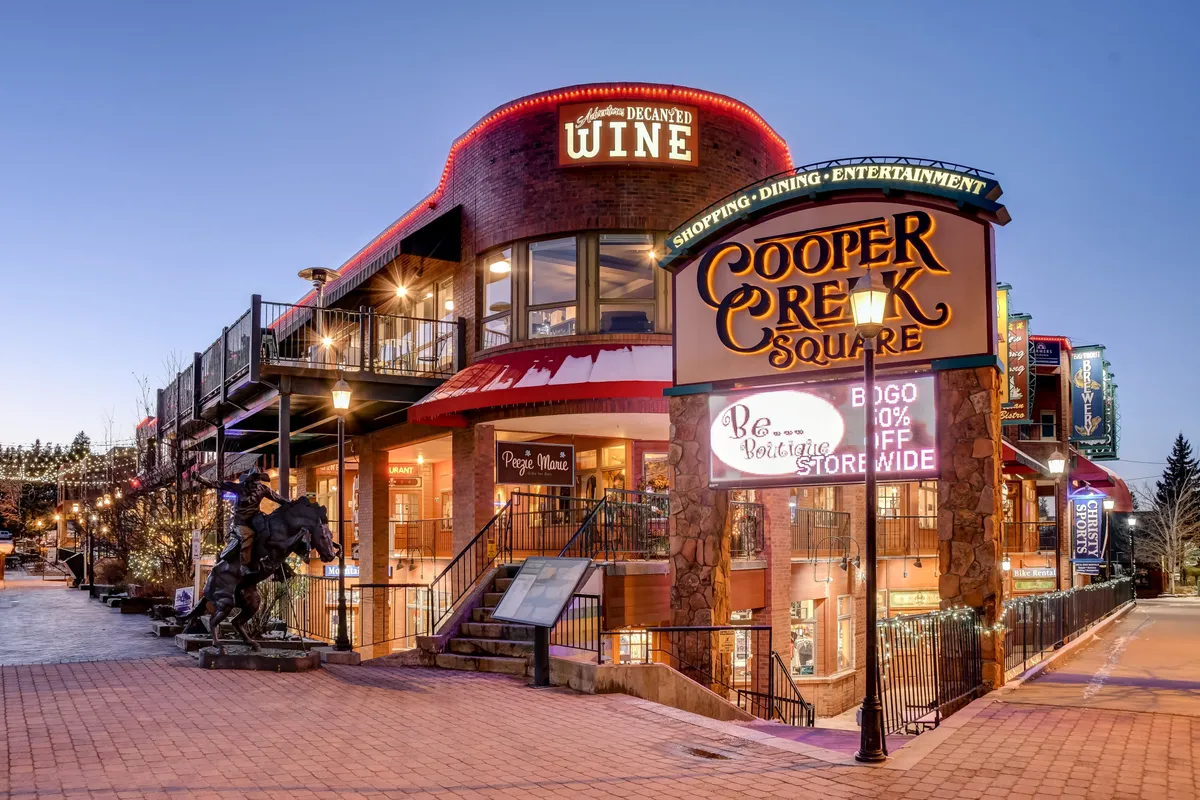 A lively exterior scene in downtown Winter Park featuring the Cooper Creek Square sign, wine shop, outdoor seating, and a festive environment. The image suggests vibrant nearby activities such as shopping, dining, and socializing in a clean, open-air community setting.