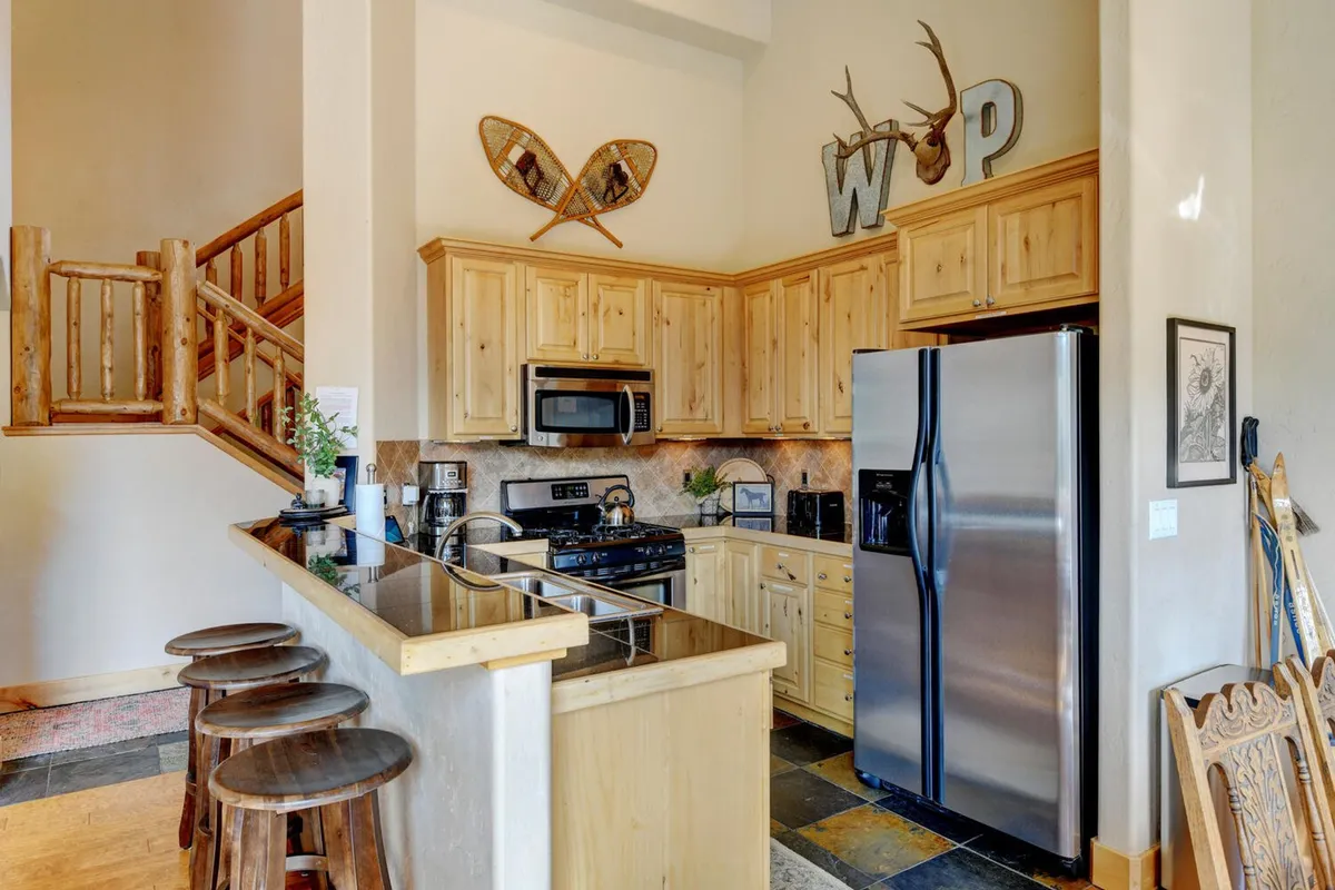 The kitchen is the star in this image, featuring a central island, stainless steel appliances, warm wooden cabinetry, and rustic decorative touches like antlers. The open-plan layout allows for easy interaction between the kitchen and adjacent living/dining spaces.