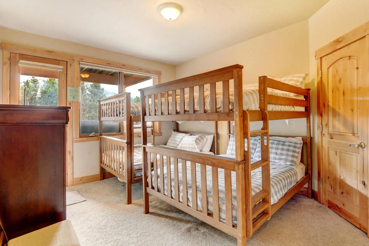 A welcoming bunk room with two full-over-full bunk beds, large windows that allow sunlight to stream in, and sturdy wooden furniture. The arrangement provides ample sleeping space and a playful yet cozy environment perfect for children or teens.