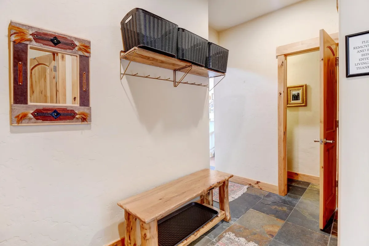 A welcoming entryway featuring a wooden bench, decorative mirror, and storage baskets. The doorway opens to the rest of the home, and the setup suggests a practical space for removing boots and storing outdoor gear after returning from mountain adventures.