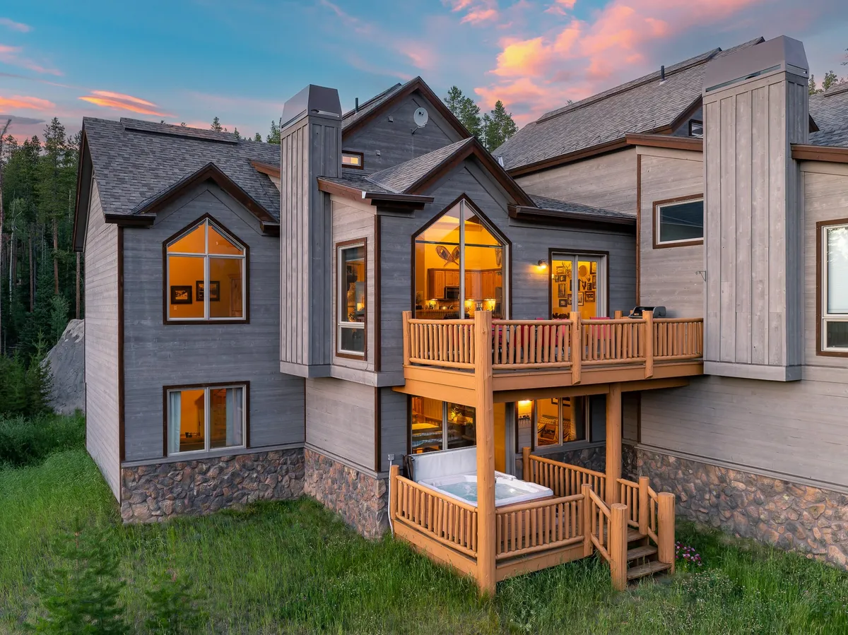 A private Jacuzzi on the deck with large windows revealing cozy interiors, and a wooden balcony set against a tranquil natural backdrop. The setting evokes rejuvenation and relaxation with sweeping sunset or starlit views.
