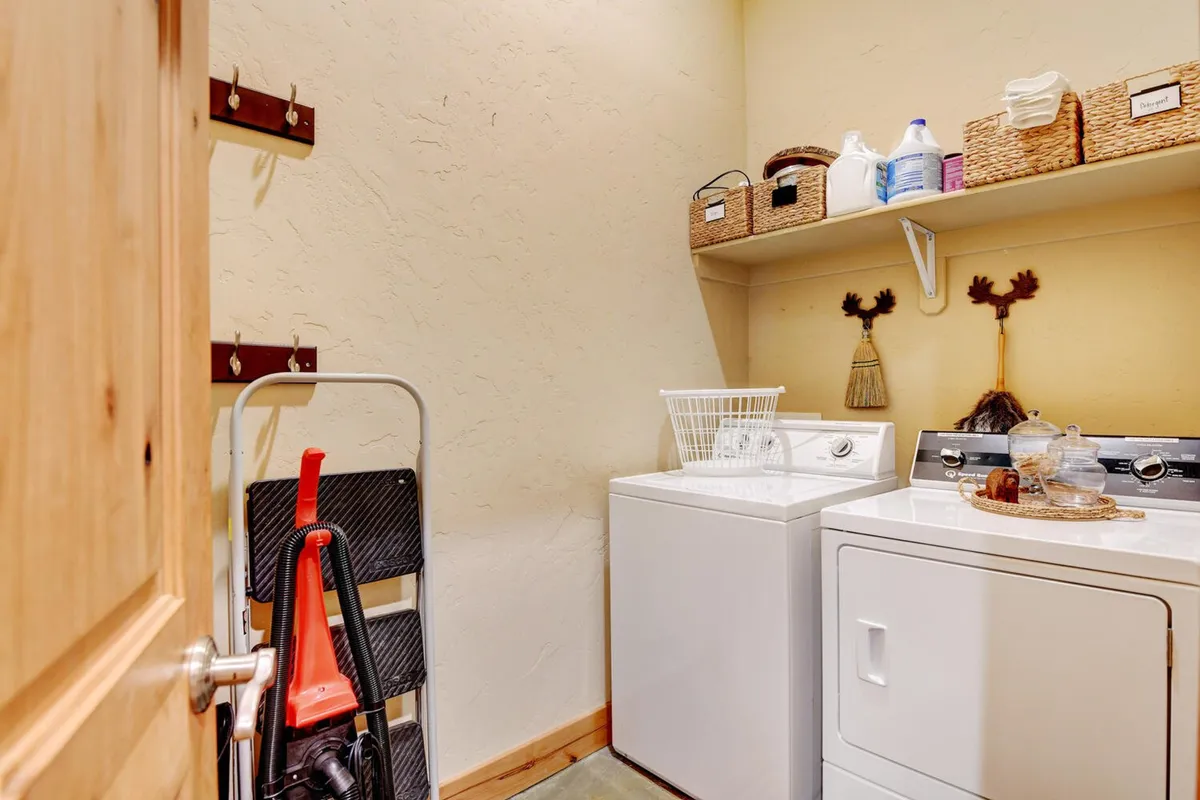 A bright laundry room equipped with a washer and dryer, shelves filled with storage baskets, and cleaning supplies. The room is tidy and purposefully arranged, promoting ease and efficiency for handling laundry needs.