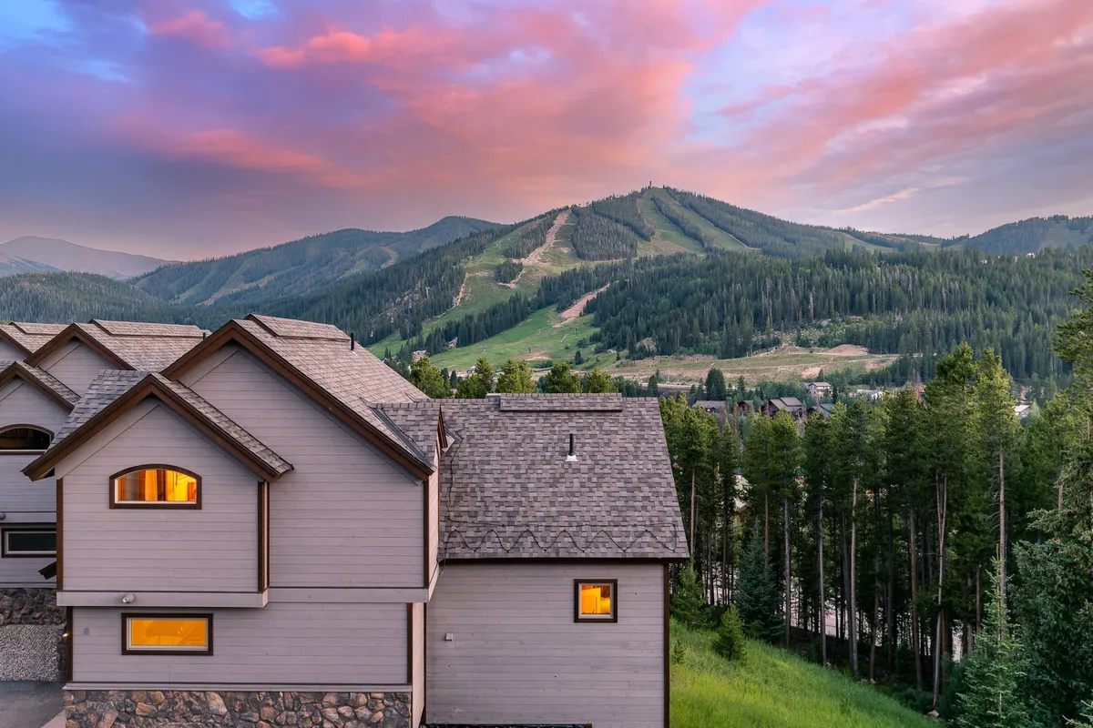 A tranquil exterior view of the home set against a stunning mountain landscape, with a sunset sky illuminating the wooded surroundings and showcasing the home's architecture. The scene radiates peace and a connection to nature, emphasizing the clean, fresh mountain air.