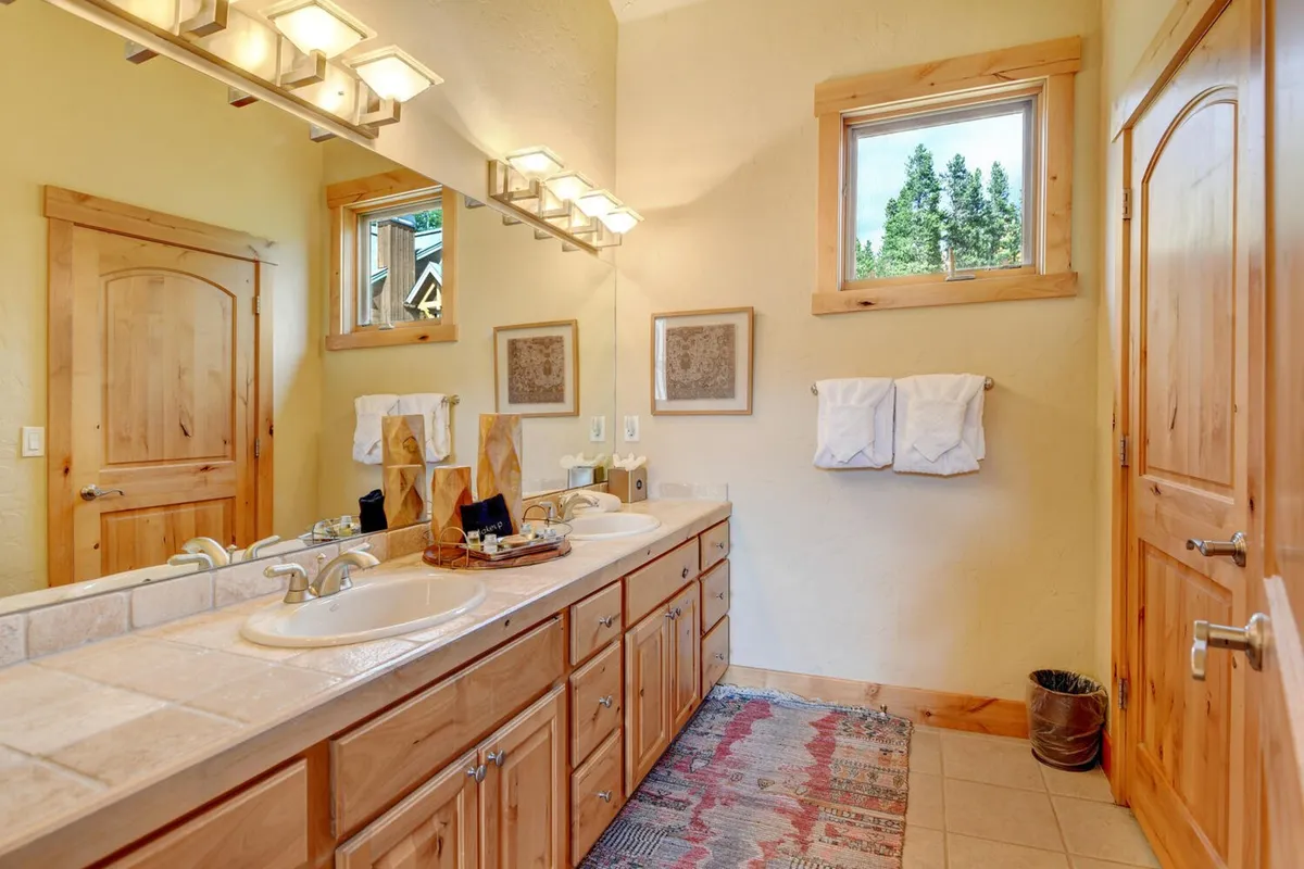 A luxurious bathroom with dual sinks, elegant wooden cabinetry, large mirrors, and a window bringing in soothing natural light. The space is designed for both functionality and self-care, offering a calm, spa-like atmosphere.