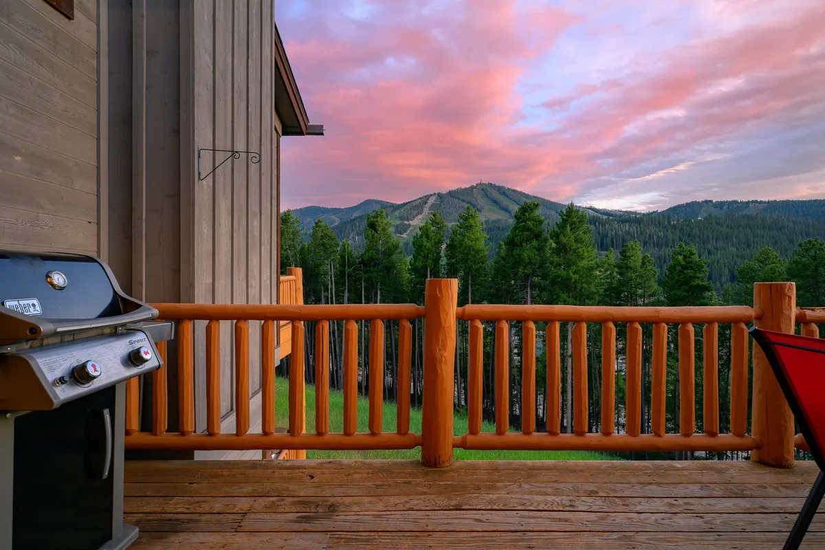 An inviting outdoor deck scene with a grill, wooden railing, panoramic mountain views, and a sunset sky—suggesting a perfect spot for BBQs, outdoor dining, and gathering with friends against a stunning natural backdrop.