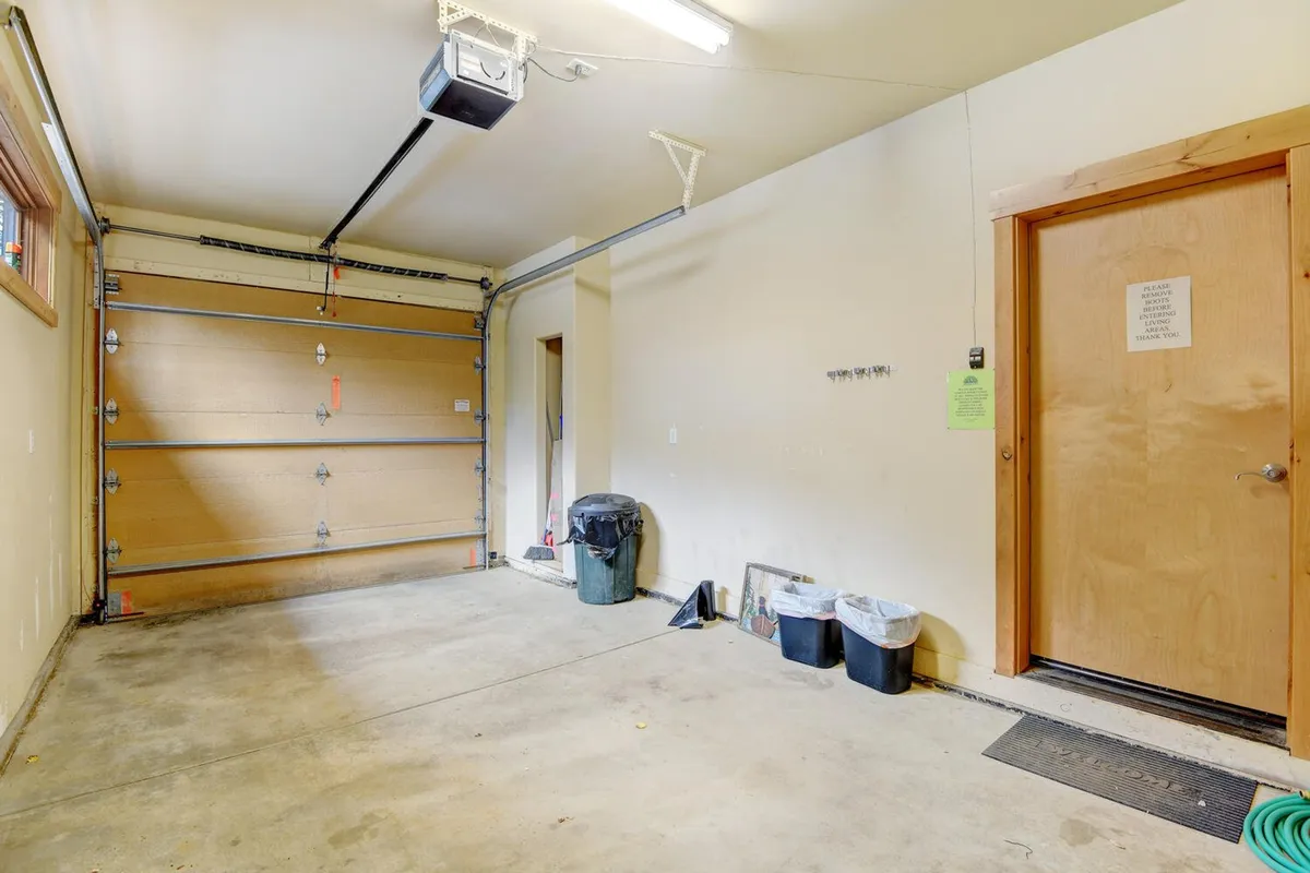 A garage interior with a visible garage door, side door, and garbage can. The open area suggests ample space for storing vehicles and outdoor equipment, with potential for organizing tools or seasonal gear.