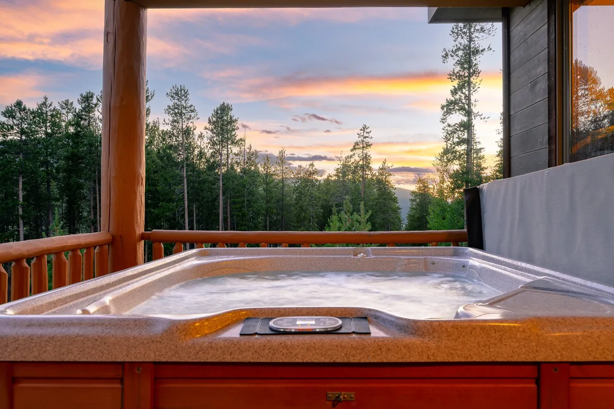An inviting outdoor hot tub nestles amongst trees under a sunset sky. The tranquil setting is perfect for unwinding after a day of adventure, with steam rising and nature surrounding the tub, offering privacy and a sense of luxury.